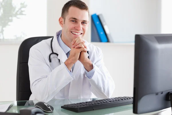 Усміхнений лікар сидить за своїм столом — стокове фото