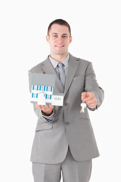 Retrato de um empresário sorridente mostrando uma casa em miniatura e — Fotografia de Stock