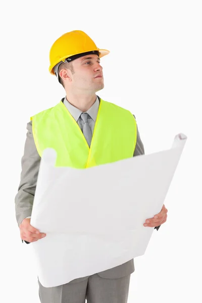 Retrato de um jovem construtor olhando ao redor enquanto mantém um plano — Fotografia de Stock