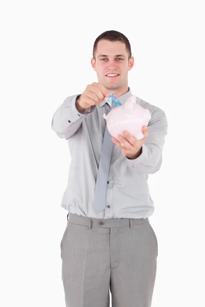 Retrato de um jovem empresário colocando uma nota em um banco porquinho — Fotografia de Stock