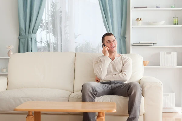 Mann telefoniert, während er auf seinem Sofa sitzt — Stockfoto