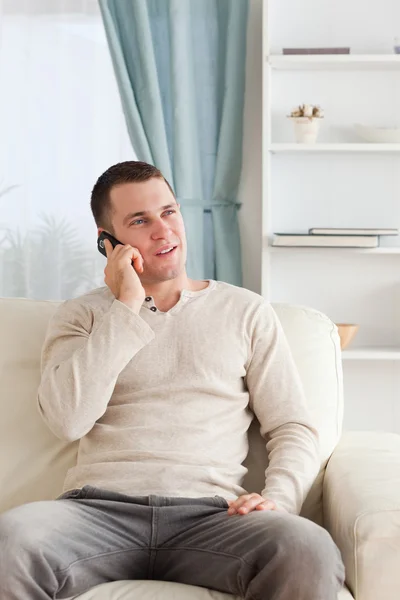 Retrato de un joven en el teléfono mientras está sentado en su sofá — Foto de Stock