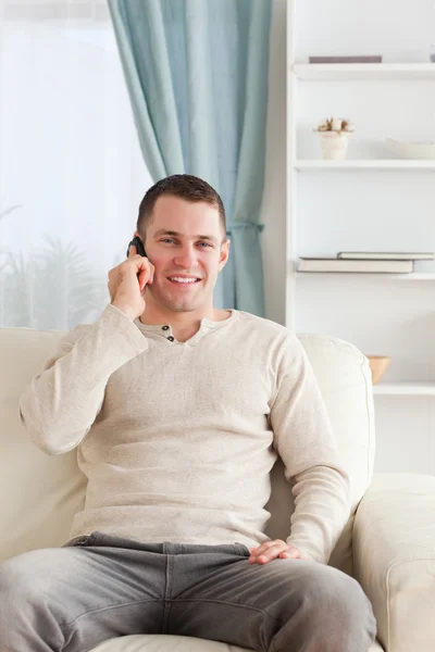 Retrato de un joven en el teléfono mientras está sentado en su sofá —  Fotos de Stock