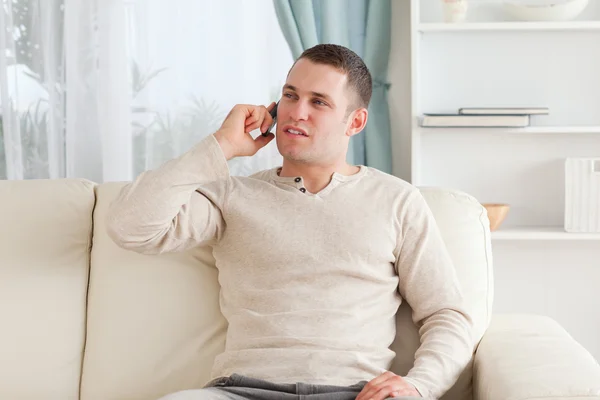 Junger Mann am Telefon, während er auf seiner Couch sitzt — Stockfoto