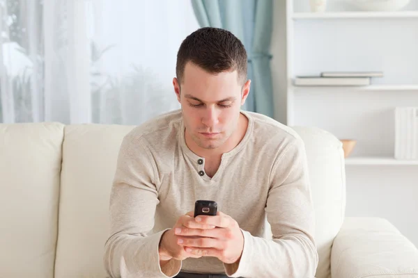 그의 소파에 앉아있는 동안 문자 메시지를 보내는 남자 — 스톡 사진