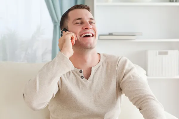 Riendo hombre haciendo una llamada telefónica mientras está sentado en un sofá — Foto de Stock