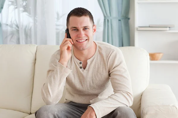 Hombre guapo haciendo una llamada mientras está sentado en un sofá — Foto de Stock