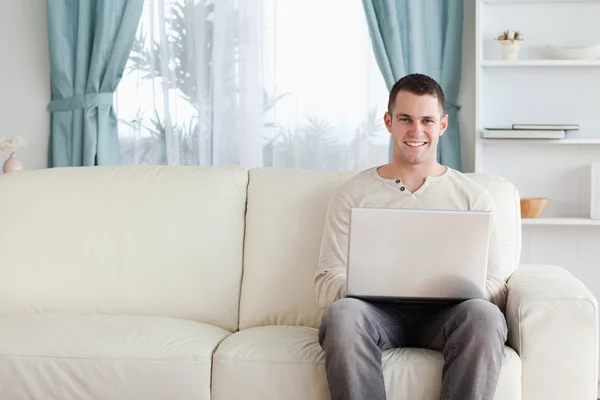 男子坐在一张沙发上的同时使用一台笔记本电脑 — 图库照片