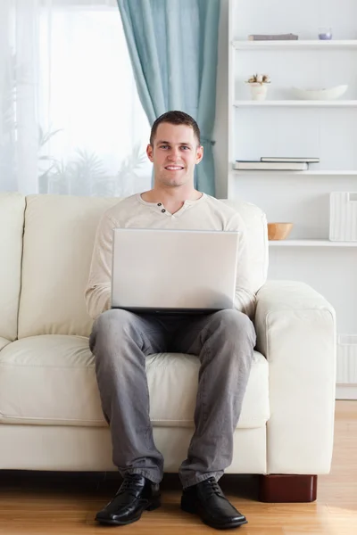 Retrato de un hombre usando un portátil mientras está sentado en un sofá — Foto de Stock