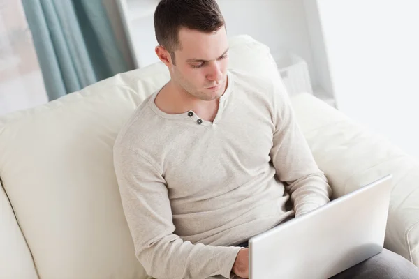 男子坐在沙发上的同时使用一台笔记本电脑 — 图库照片