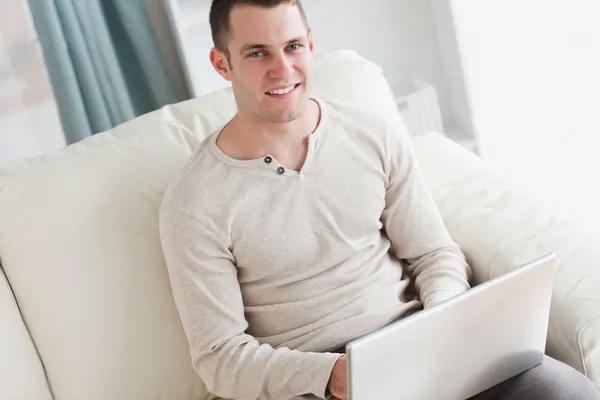 Усміхнений чоловік використовує ноутбук, сидячи на дивані — стокове фото