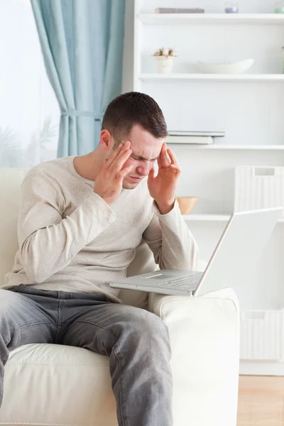 Bir dizüstü bilgisayar kullanırken bir baş ağrısı olan bir adam portresi — Stok fotoğraf
