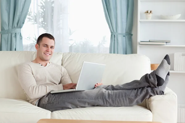 Hombre sonriente relajándose con un portátil — Foto de Stock