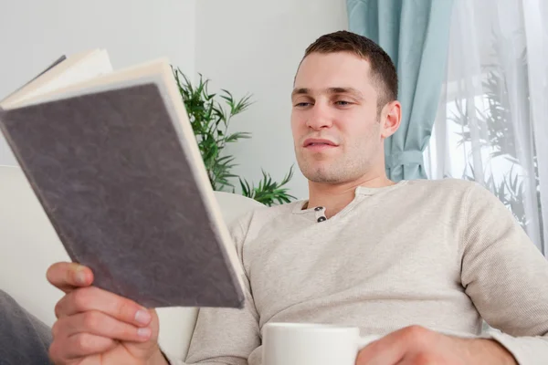 Homme lisant un livre tout en tenant une tasse de thé — Photo
