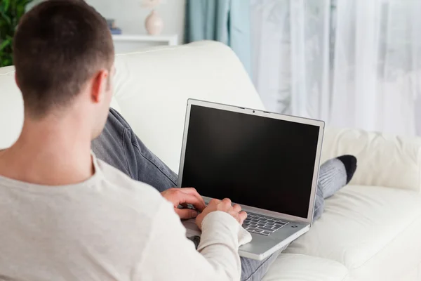 人坐在沙发上躺在使用一台笔记本电脑 — 图库照片