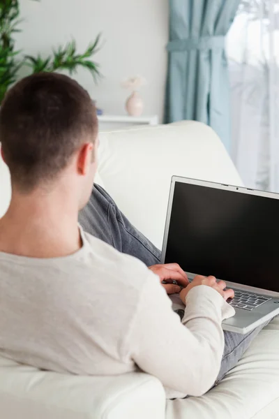 Porträt eines Mannes, der auf seinem Sofa liegt, um einen Laptop zu benutzen — Stockfoto