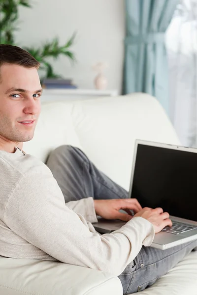 Porträt eines Mannes, der mit einem Laptop auf seinem Sofa liegt — Stockfoto