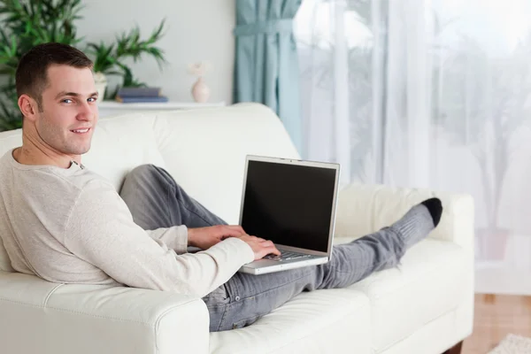 Мужчина лежит на диване с ноутбуком — стоковое фото