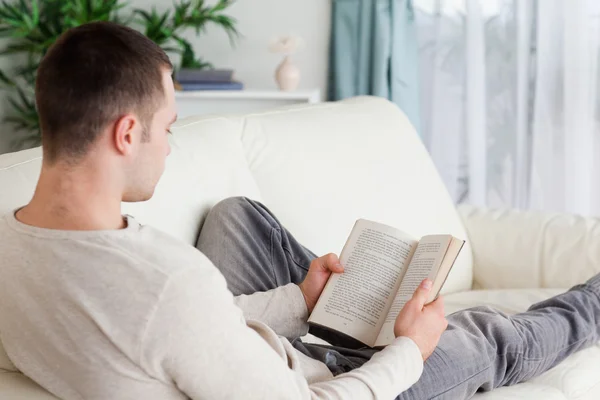 Portrait d'un homme allongé sur son canapé lisant un livre — Photo