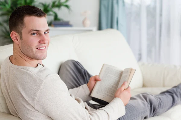 Portrait of a man lying on his couch holding a book — Stock Photo, Image