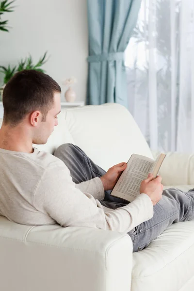 Portrait d'un homme allongé sur un canapé lisant un livre — Photo