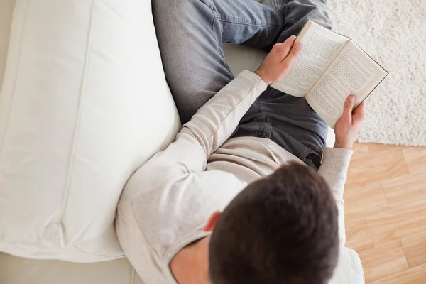 Человек, лежащий на диване и читающий книгу — стоковое фото