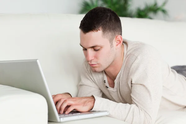 男人躺在一张沙发，使用一台笔记本电脑 — 图库照片