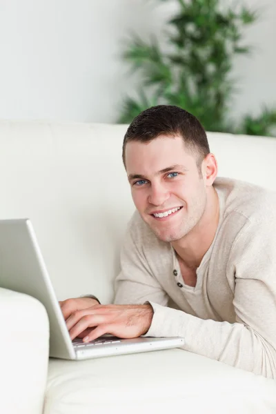 Portrait of a man lying on a sofa with a laptop — Stock Photo, Image