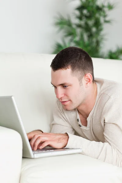 Portrait of a man lying on a sofa using a laptop — Stock Photo, Image