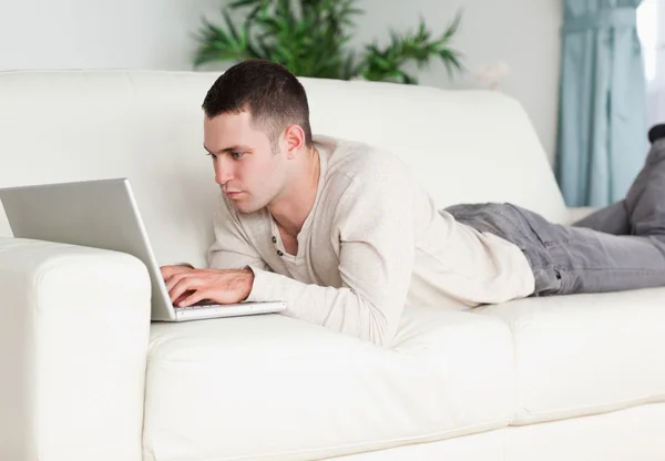 Junger Mann liegt mit Laptop auf Sofa — Stockfoto