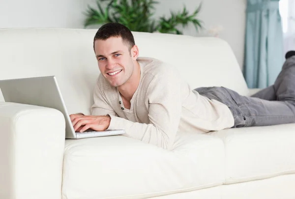 Улыбающийся мужчина лежит на диване с ноутбуком — стоковое фото