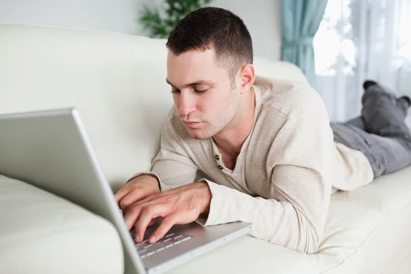 Сосредоточенный мужчина лежит на диване с ноутбуком — стоковое фото