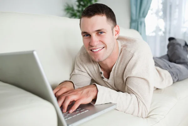 微笑的人躺在沙发上用一台笔记本电脑 — 图库照片