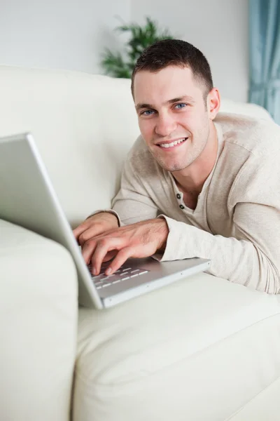 Προσωπογραφία άνδρα χαμογελώντας ξαπλωμένη σε έναν καναπέ με ένα laptop — Φωτογραφία Αρχείου