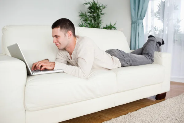 Bir dizüstü bilgisayar kullanarak bir kanepede yatan yakışıklı adam — Stok fotoğraf