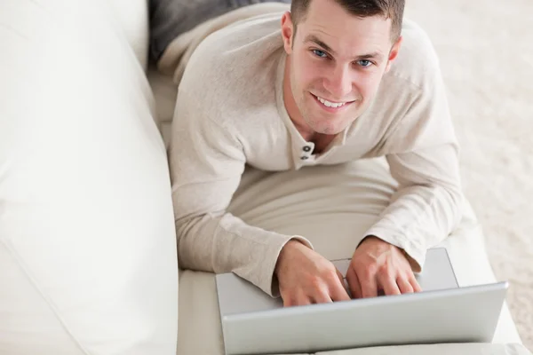 Szczęśliwy człowiek leży na kanapie z notebookiem — Zdjęcie stockowe