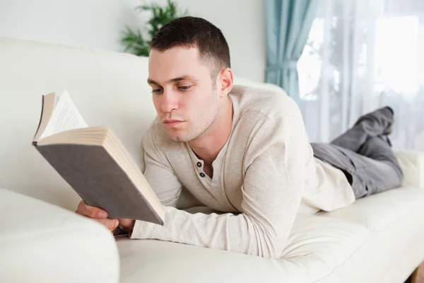 男はソファに横になっている本を読む — ストック写真