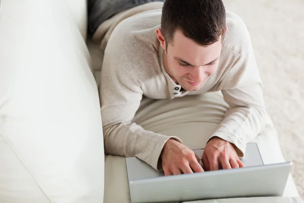 Ung man liggande på en soffa att använda en bärbar dator — Stockfoto