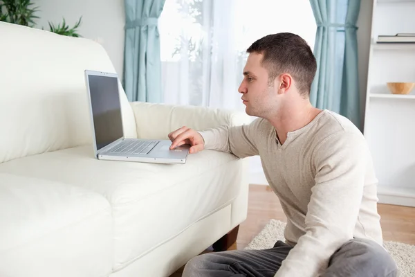 Bir dizüstü bilgisayar kullanırken bir halı üzerinde oturan adam — Stok fotoğraf