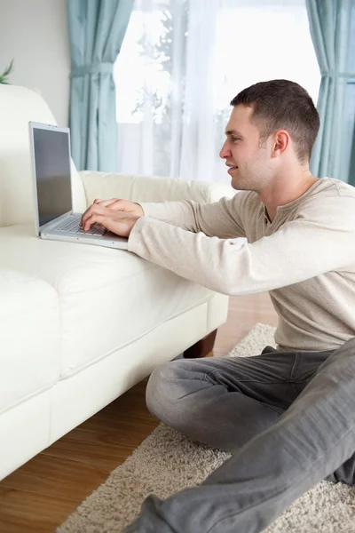 Portrait of a smiling man sitting on a carpet while using a lapt — Stock Photo, Image