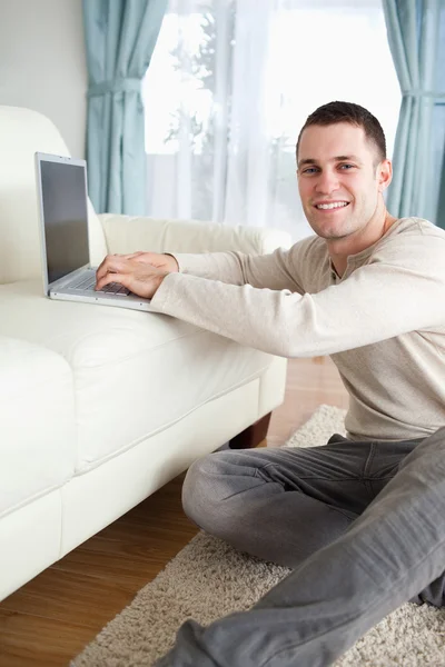 Ritratto di un uomo sorridente seduto su un tappeto con un computer portatile — Foto Stock