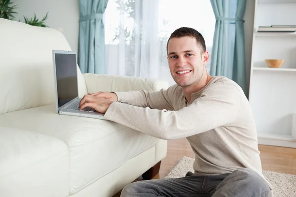 Uomo sorridente seduto su un tappeto con un computer portatile — Foto Stock