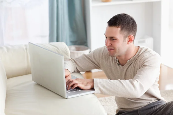 Usmívající se muž sedí na koberci při použití poznámkového bloku — Stock fotografie