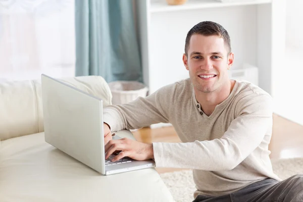 Usmívající se muž sedí na koberci pózuje s notebook — Stock fotografie