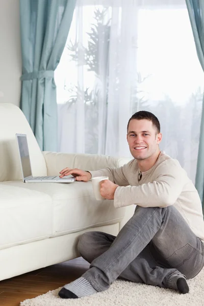 Portret mężczyzny siedzi na dywanie przy pomocy pewien laptop i gospodarstwa — Zdjęcie stockowe