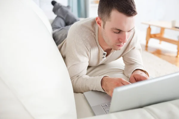 Good looking man lying on a couch using a laptop — Stock Photo, Image