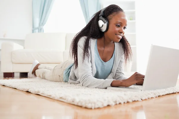 Donna sdraiata sul pavimento con il suo computer portatile godendo la musica — Foto Stock