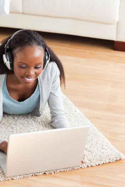 Close up of woman lying on floor with laptop listening to music — Stock Photo, Image
