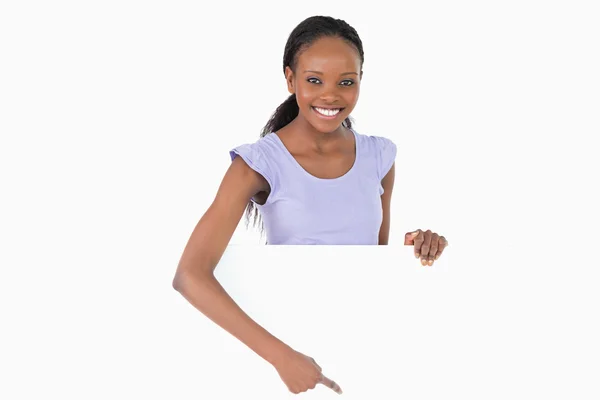Woman pointing on placeholder beneath her on white background — Stock Photo, Image