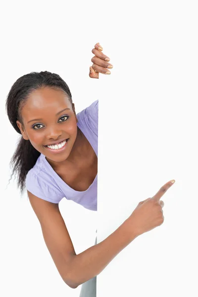 Young woman looking around the corner pointing at something on w — Stock Photo, Image